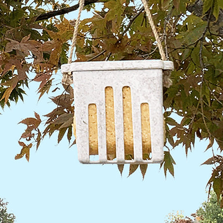 Nut Husks Suet Cake Feeder hanging on a tree branch, featuring a white basket design with holes, suitable for holding suet or seed cakes.