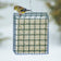 Mr. Bird Large Seed & Suet Block Cage with chain, filled with seeds, supports an American goldfinch perched on top, showcasing its durable wire-cage design.