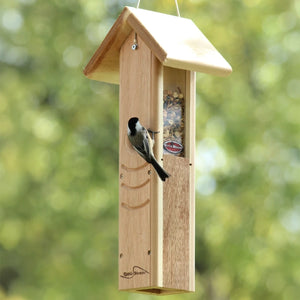 Black-capped chickadee feeding from a hanging cedar mealworm feeder with protective roof.