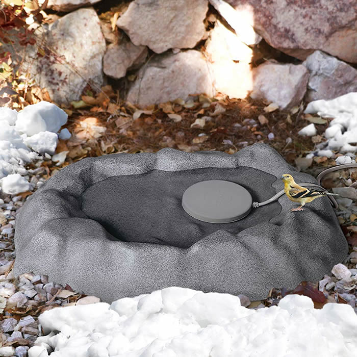 Ground Thermo-Birdbath 80 Watts, Gray: Yellow bird perched on rock, showcasing heated birdbath maintaining ice-free water in winter, made from durable plastic resin with stonelike appearance.