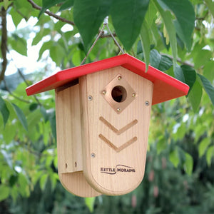 Cedar hanging birdhouse with red recycled plastic roof displayed in a backyard tree.