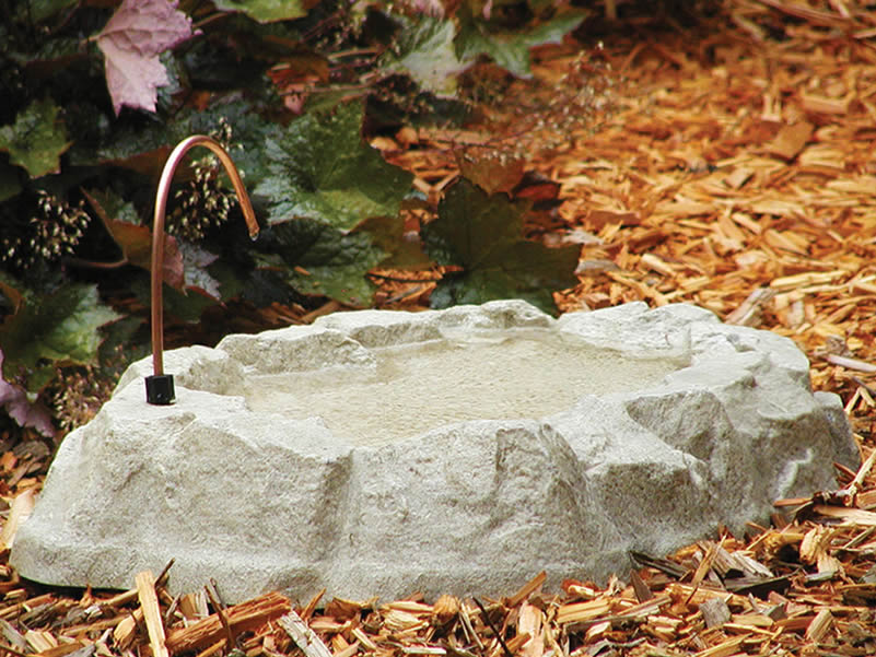 Rocky Mountain Bath & Dripper: Realistic granite fiberglass bird bath with built-in dripper, set in a garden with surrounding rocks and leaves.