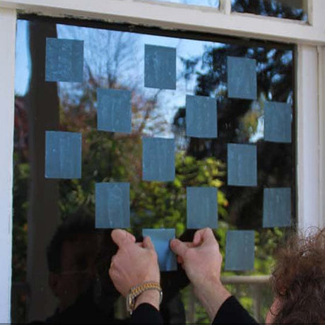 Person applying ABC 3 Inch Pre-Cut Tape Blocks to a window to prevent bird collisions, showcasing usage of translucent, easy-to-apply bird-saving tape.