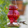 Ruby Visions Antique Glass Gravity Hummingbird Feeder with red textured glass, white flower-shaped ports, and a hummingbird feeding.