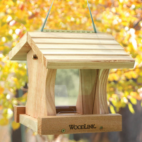 Deluxe Cedar Hopper Feeder, Mini: Wooden bird feeder with a sloped roof, plastic sides for seed viewing, and two feeding trays. Hangs by a cable from a tree.