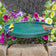 Ground Level Bird Bath, Green: Yellow bird with black and white feathers perched on the birdbath rim, surrounded by garden flowers and greenery.