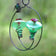 Balance 2 Hummingbird Feeder, Green, with two red flower feeding tubes and a handblown recycled glass reservoir, hanging on a wire with a hummingbird perched.