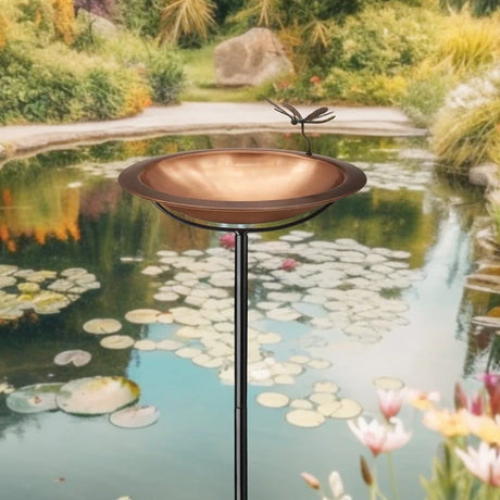18 Torched Copper Basin With Fairy features a copper-toned birdbath with a dragonfly on its rim, set on a sleek black pole.