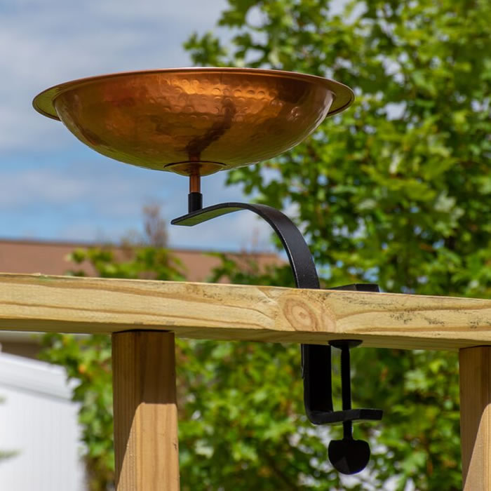 Rail Mounted Hammered Copper Bird Bath on wooden railing, featuring a hammered copper basin and black wrought iron deck mount. Perfect for birds to drink and bathe.