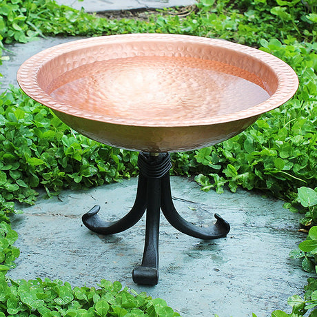 Hammered Solid Copper Bird Bath with Tripod Stand, featuring a 2-3/4 inch deep basin, displayed outdoors on sturdy wrought iron stand in a garden setting.