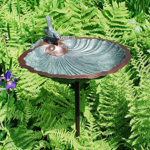 Scallop Shell Bird Bath with Stake in a garden, featuring embossed basin and decorative songbird on rim, supported by a sectional wrought iron stake.