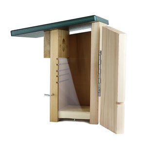 A wooden bird house with an open door, showing a light natural wood body, silver metal hinges, a green roof, and a white interior perch, isolated on a white background.