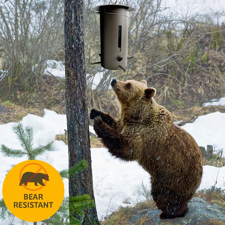 Bear standing beneath a hanging Bear Proof Bird Feeder in a snowy woodland, with a bear-resistant badge.