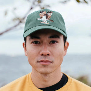 Man wearing the Bird Collective Osprey Hat, Pine, featuring an embroidered Osprey logo and adjustable strap for a secure fit.