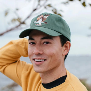 Man wearing the Bird Collective Osprey Hat, Pine, with an embroidered Osprey logo, adjustable strap, and classic design for birdwatching or daily wear.