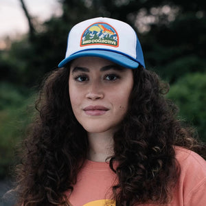 HawkWatch Trucker Hat, Blue Jay: Woman with long curly hair wearing a stylish cap featuring a white front and breathable mesh back.