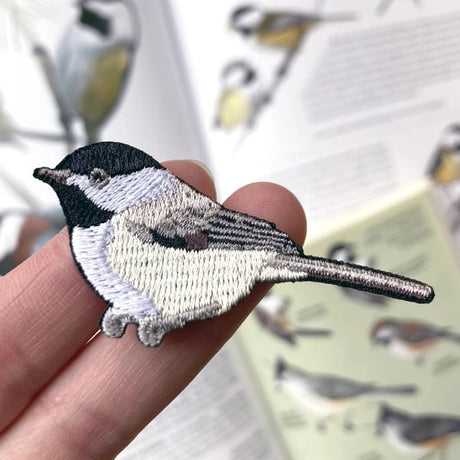 Person holding Bird Collective Black-capped Chickadee Patch, showcasing intricate embroidery of the bird, ideal for backpacks, jackets, and hats.