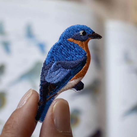 Bird Collective Eastern Bluebird Patch held in hand, showcasing intricate embroidery and iron-on backing for easy attachment to clothing or accessories.