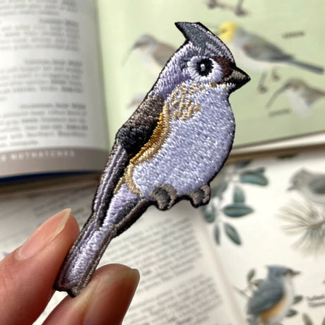 Person holding a detailed Bird Collective Tufted Titmouse Patch, showcasing intricate embroidery. Ideal for jackets, backpacks, or hats with an iron-on backing.