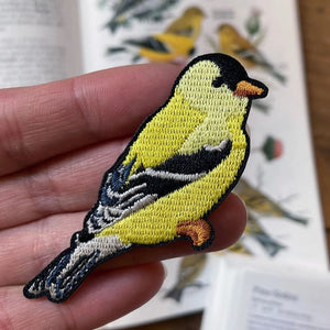 Bird Collective American Goldfinch Patch held in hand, showcasing detailed embroidery of a yellow bird, perfect for customizing clothing and accessories.