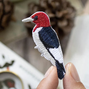 Bird Collective Red-Headed Woodpecker Patch in hand, showcasing intricate embroidery and iron-on backing for easy attachment to clothing or accessories.