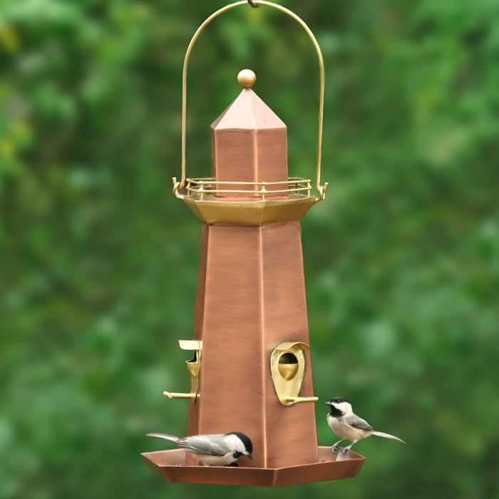 Lighthouse Bird Feeder with brass and copper finishes, featuring three perches, a spacious base tray, and two birds feeding.