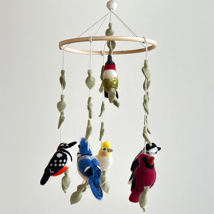 Felt Bird Wings Mobile featuring handcrafted wool-felt birds like cardinal, hummingbird, blue jay, chickadee, and parrot on a wooden frame with decorative leaves.