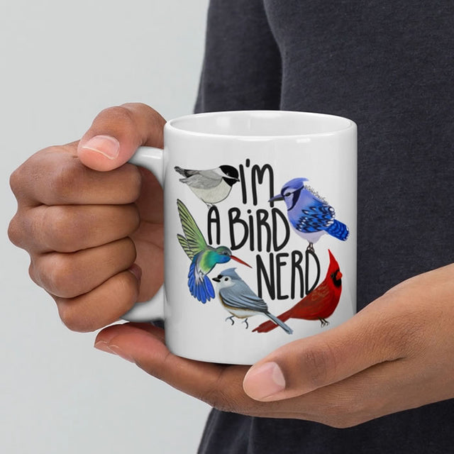 Person holding I'm A Bird Nerd ceramic mug featuring hand-drawn birds like Chickadee, Titmouse, Hummingbird, Cardinal, and Blue Jay. Dishwasher and microwave safe.