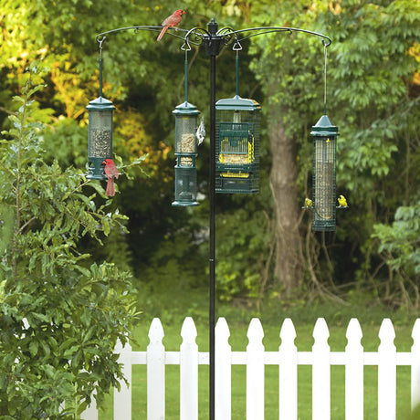 BirdsUP Versa Pole System with multiple bird feeders hanging from a sturdy pole, set up amidst outdoor surroundings with trees and a fence in the background.