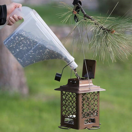 SureFill Super Tote being used to pour seeds into a bird feeder, showcasing its easy-to-grip handle and tapered spout for efficient seed distribution.