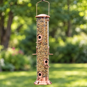 Copper tube bird feeder filled with mixed bird seed, featuring multiple feeding ports and perches, hanging in a lush green backyard.