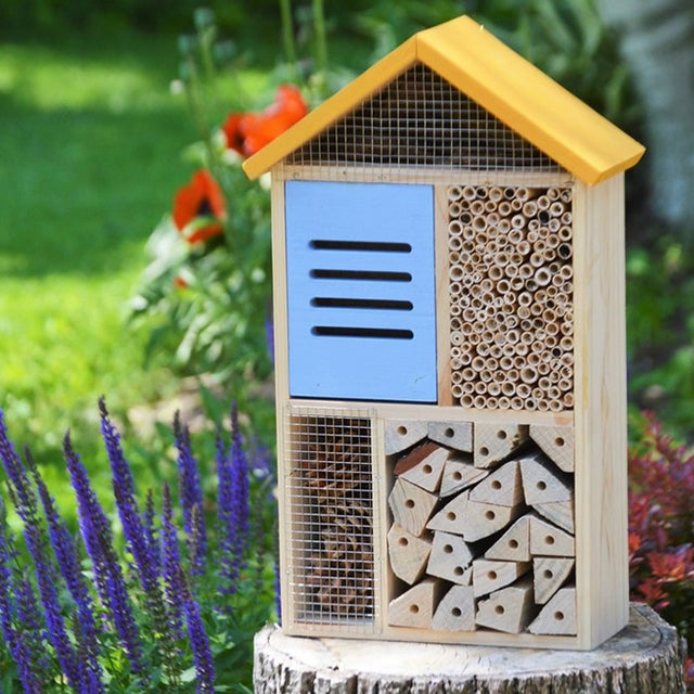 Cedar Deluxe Insect House on a stump, featuring multiple compartments for bees and ladybugs, designed to attract birds and provide natural pest control.