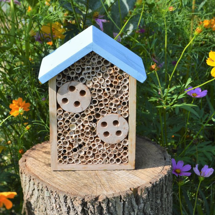 Cedar Bee House on a stump, featuring circular nesting holes and an overhanging roof, designed to attract Mason and Leafcutter Bees for garden pollination.