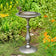 Classic Pewter Pedestal Bird Bath with Fairy featuring a round basin on a pedestal, surrounded by green foliage and orange flowers in a garden setting.
