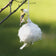 American goldfinch tugging at a Cottontail Nest Builder—a suspended ball of nesting fibers—ideal for crafting warm, dry nests.