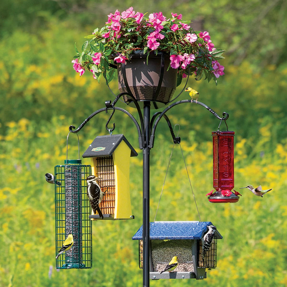 Four Arm Heavy Duty Pole with Twister & Flower Basket featuring birds on feeders and a potted plant, showcased in an outdoor setting.