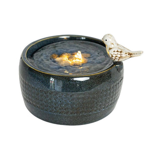 Elloise LED Bird Fountain with a distressed white bird perched on a navy blue embossed fountain, featuring LED lights and natural pebbles for a tranquil ambiance.