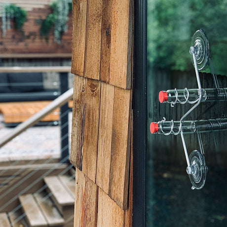 Window Hummingbird Feeder, 2 Tube Feeder with red caps, glass bottles, and aluminum frame, mounts via suction cup on a window for easy hummingbird viewing.