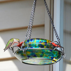 Spring Rain Illuminated Hummingbird Feeder with bird perched on decorative glass feeder; solar panel on top, three leaf-shaped perches, metal hanger, and vibrant handblown glass.