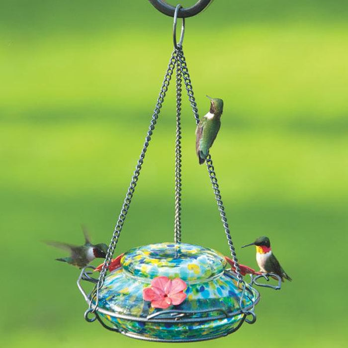 Spring Rain Illuminated Hummingbird Feeder with vibrant glass, solar-powered top, and three leaf-shaped perches, attracting birds to an outdoor decorative feeder.