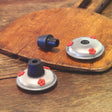 Replacement Gondola & Stopper on wooden surface, featuring a silver metal base with three red feeding ports and a rubber stopper for hummingbird feeders.