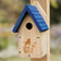 Garden Bluebird House with a blue roof, mounted on a post, features a laser-etched bluebird design and a side panel for easy cleaning.