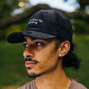 Young man wearing the I'd Rather Be Birding black corduroy hat with adjustable strap, showcasing its relaxed, unstructured fit in a park setting.