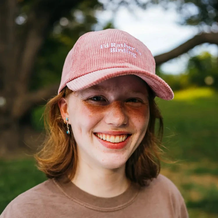 Young person smiling in a park, wearing the “I’d Rather Be Birding” pink corduroy hat with adjustable strap, showcasing their love for birding.