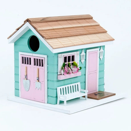 She Shed Birdhouse featuring a small bench, pink door, window box with flowers, and decorative garden tool motifs, designed as a charming bird sanctuary.