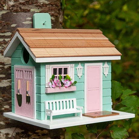 She Shed Birdhouse featuring a front bench, window box, picket fence accents, and decorative garden tools, crafted from wood with drainage and ventilation.