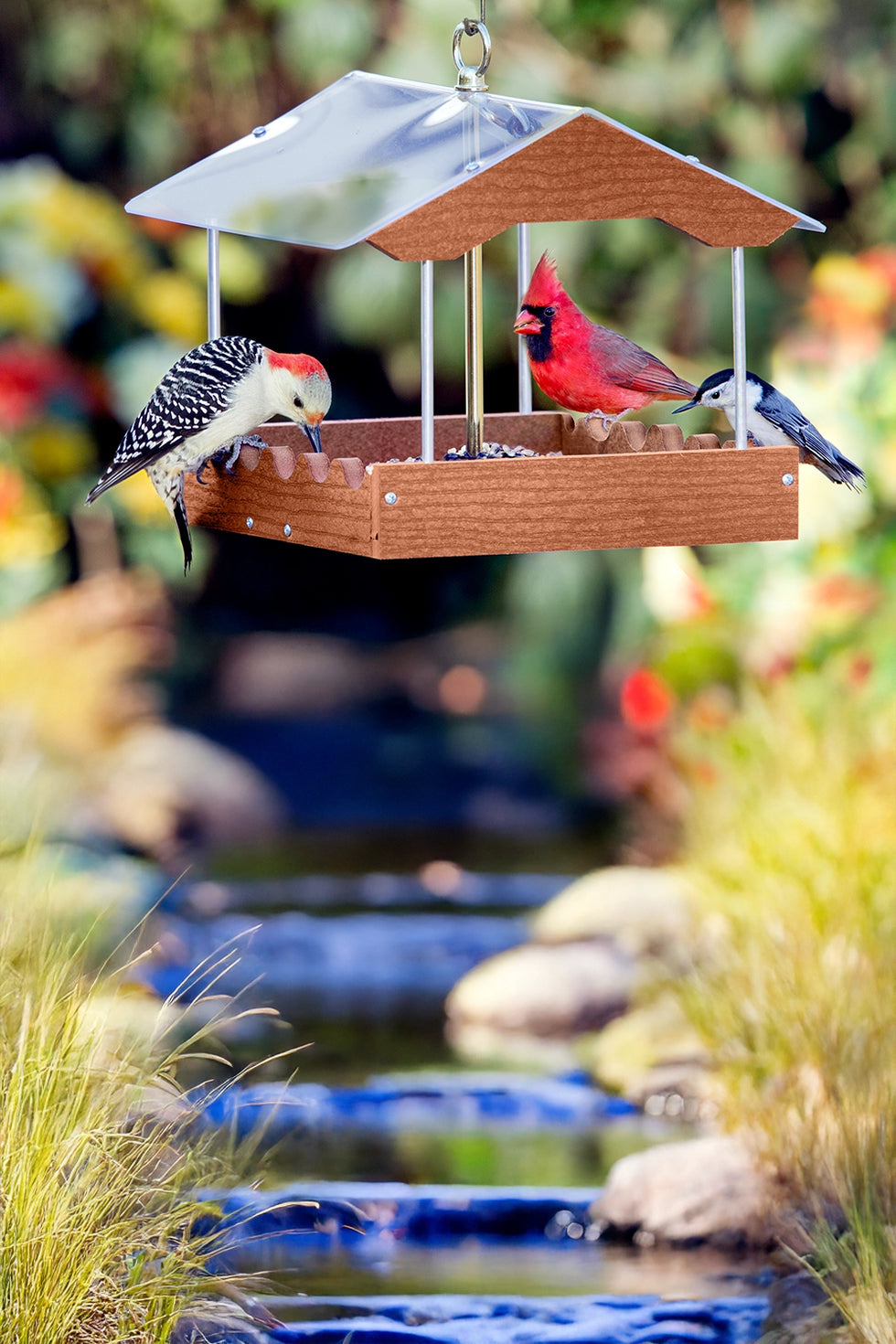 Hanging platform bird feeder with birds eating seed from a tray.  Cardinal, woodpecker and nuthatch.