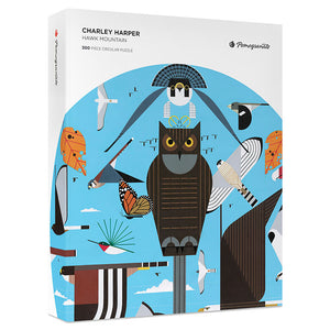 Charley Harper Hawk Mountain 500-Piece Circular Jigsaw Puzzle featuring an owl, hawks, and colorful birds in a naturalistic, cartoon-style illustration. Includes 8x10 inch reference insert.