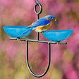 Mosaic Birds Side by Side Poppy Feeder - Bluebird Blue: A bluebird perched on a double dish feeder with red glass bowls, filled with treats, hanging on a sturdy metal hanger.