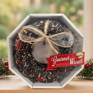 Mr. Bird Gourmet birdseed wreath with pecans and a gold bow in an octagonal gift box, displayed beside holiday greenery.